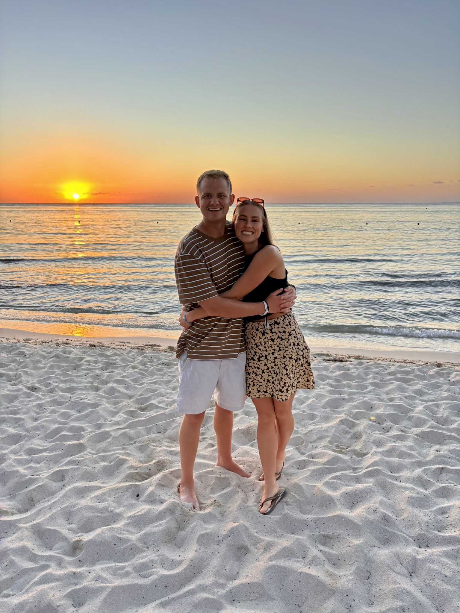 Bri and Liam standing together on the beach at sunset.